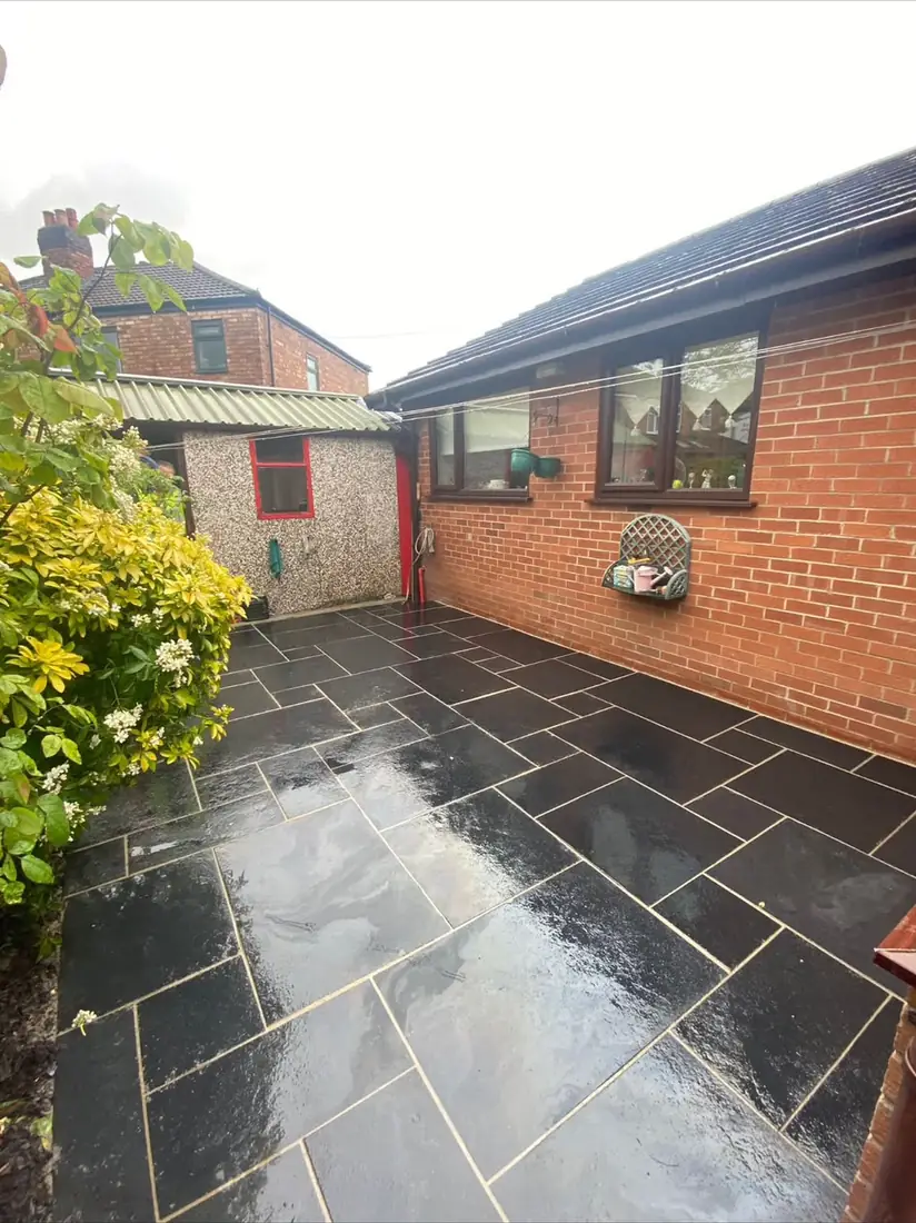 Black limestone paving laid in a random pattern across an enclosed rear yard, rain soaked