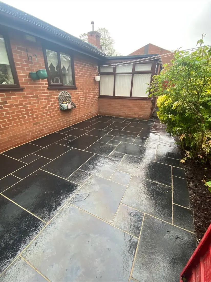 Black limestone patio paving wrapping around a brick conservatory with planted borders