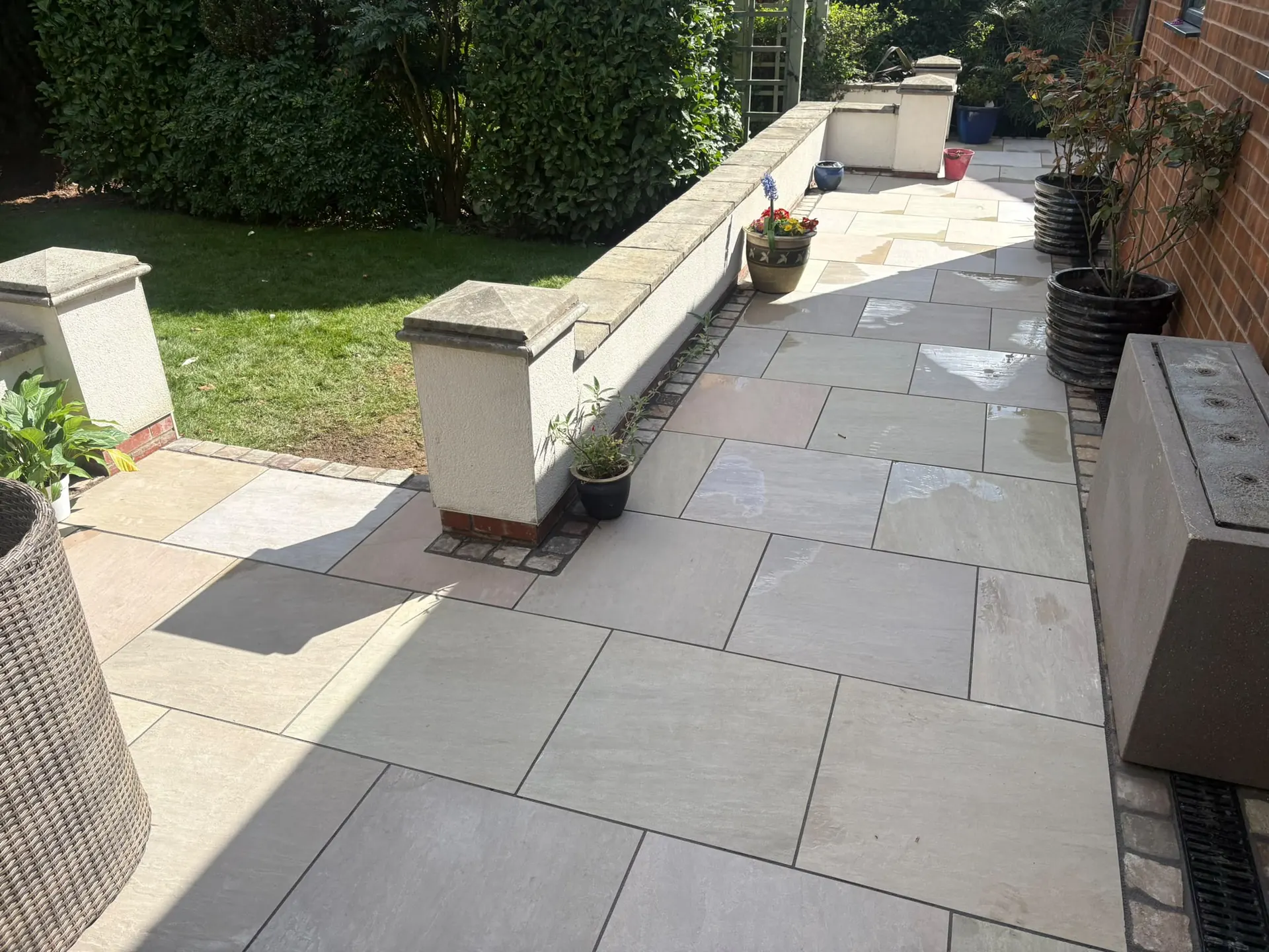 Indian sandstone patio with brick edging and a rendered retaining wall with capped piers