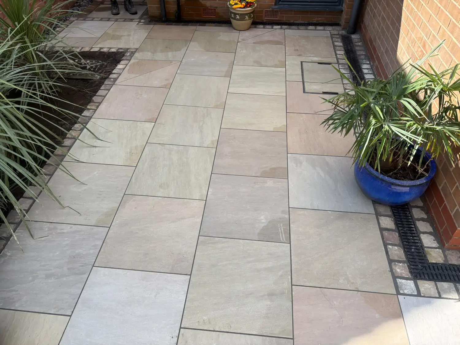 Sandstone paving with a sett bordered ACO drainage channel running along the house wall