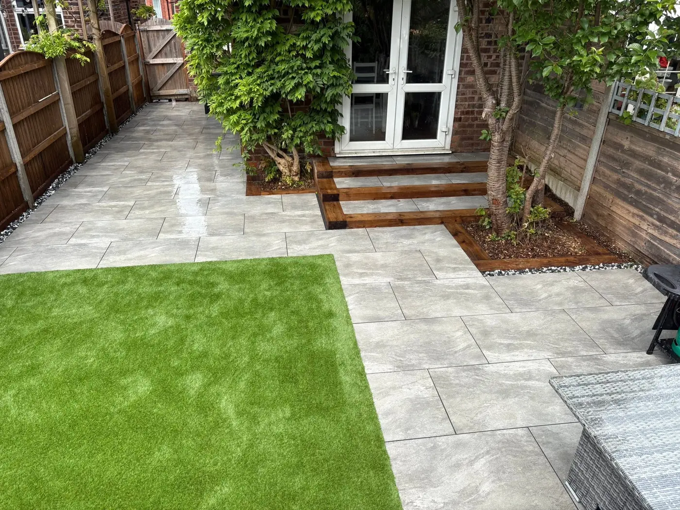 Grey porcelain patio with timber sleeper steps and a new artificial lawn in a rebuilt rear garden