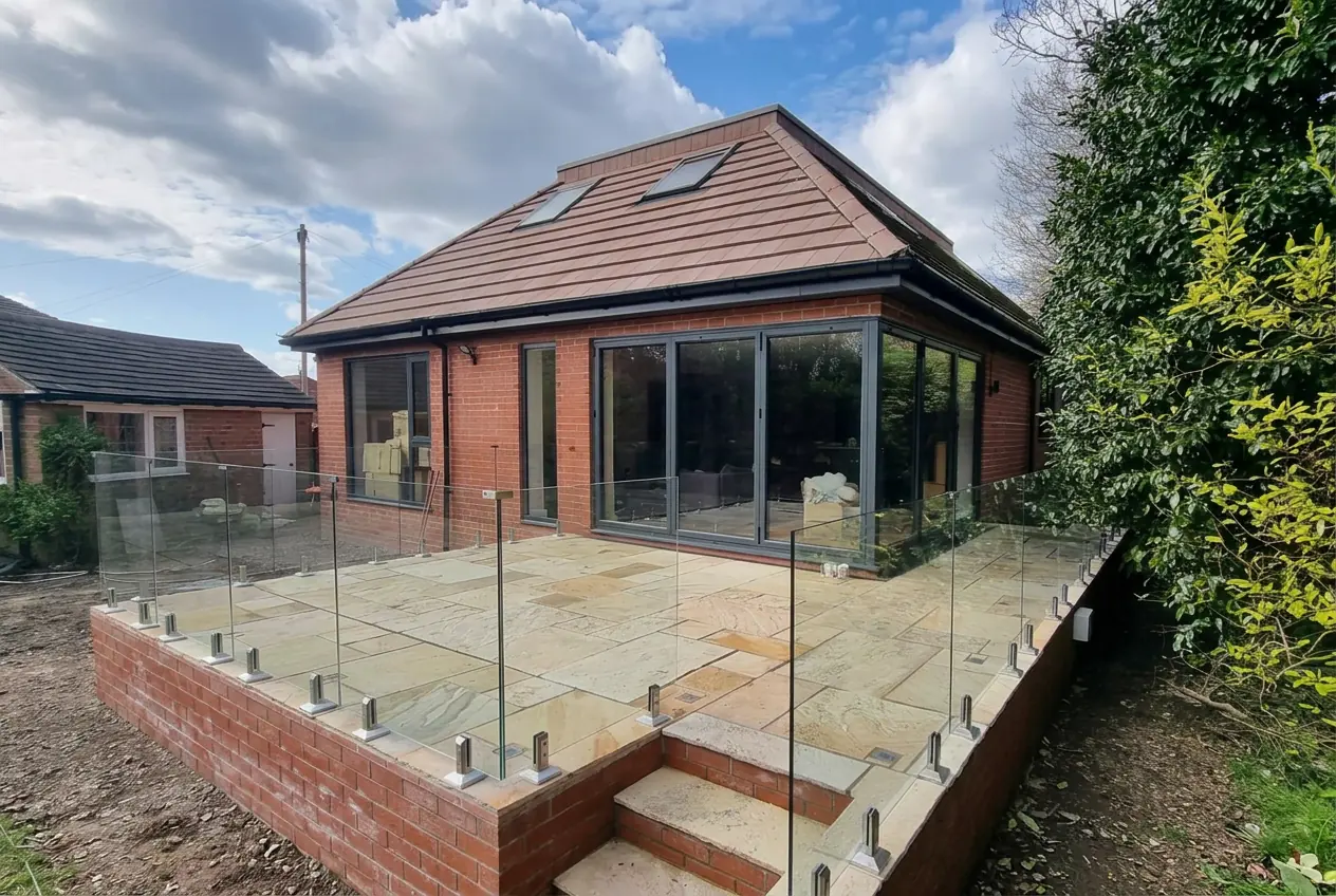 Raised sandstone patio on brick retaining walls with a frameless glass balustrade and steps
