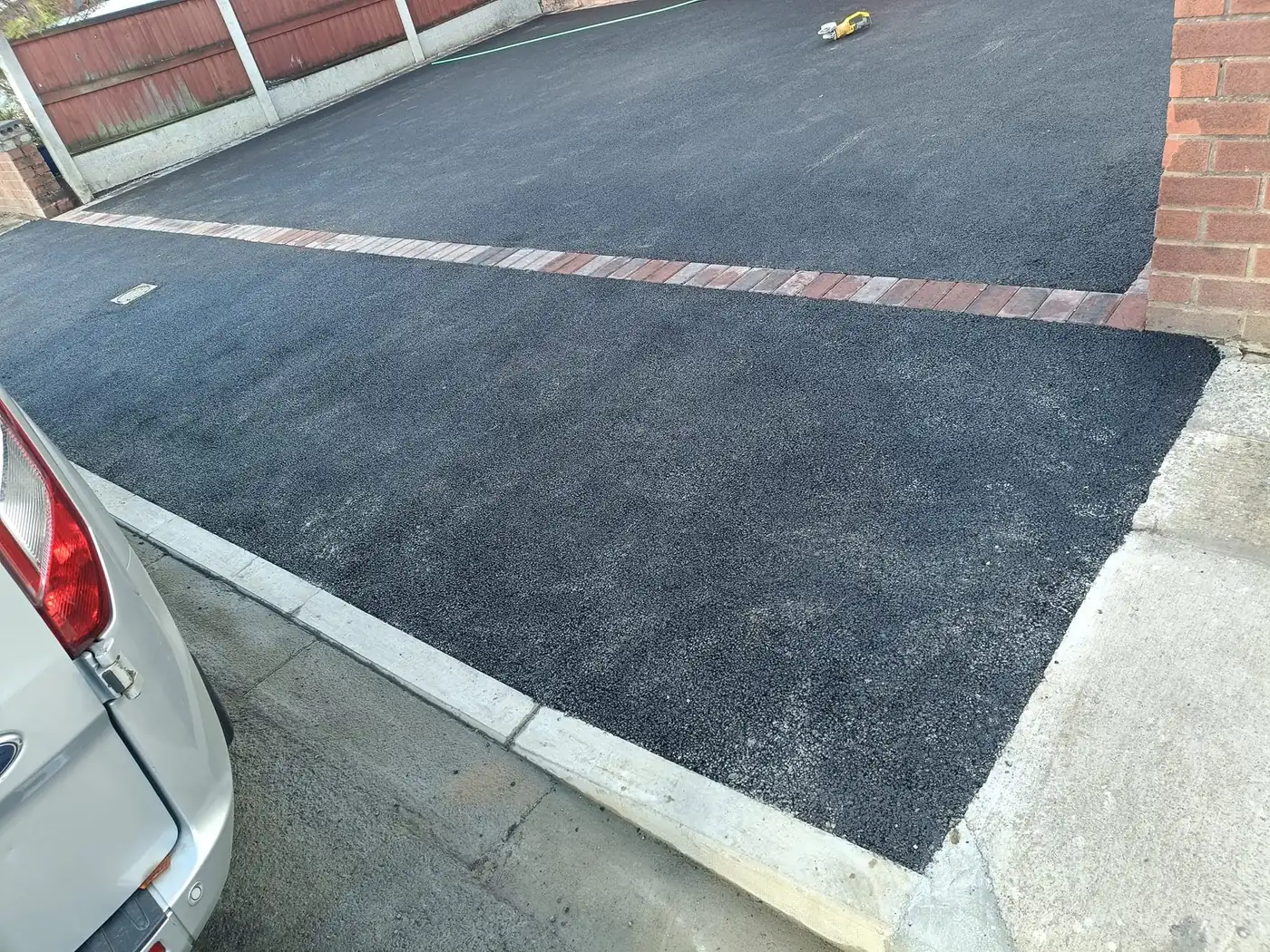 Freshly laid tarmac driveway with a clay brick sett border and concrete kerb edging
